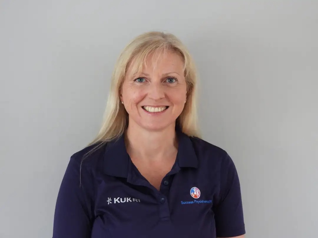 WhatsApp Image 2023-08-07 at 4.01.00 PM Hazel Lee wearing navy poloshirt with Success Physiotherapy insignia, long blonde hair is down and she is smiling